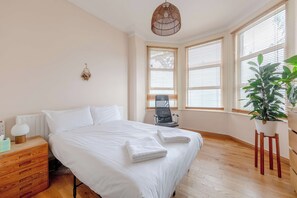 Une chambre à coucher avec un lit, une table de chevet, une chaise, une plante en pot et de grandes fenêtres.