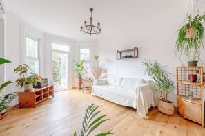 Un salon spacieux avec un canapé blanc, un plancher en bois et diverses plantes en pot.