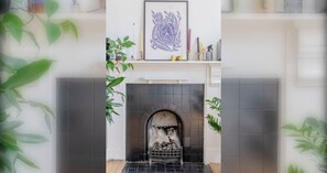 Una chimenea con una obra de arte enmarcada encima, rodeada de plantas en macetas.