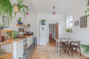 Une cuisine moderne avec des meubles en bois, une cuisinière à gaz et un réfrigérateur. On y trouve également des plantes suspendues et un coin repas avec une table et des chaises.
