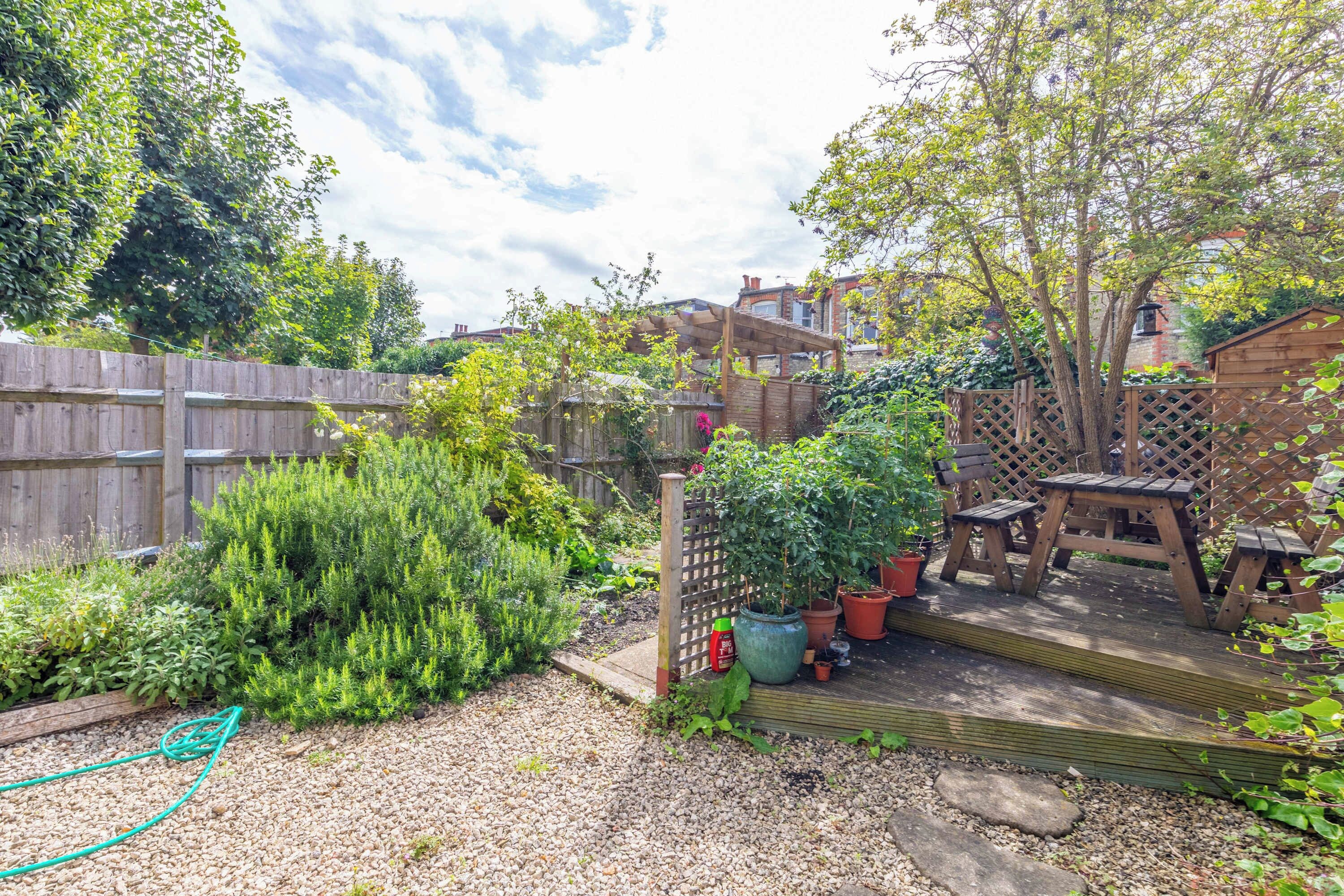 Un jardin avec une terrasse en bois, des plantes en pot et une clôture en bois.