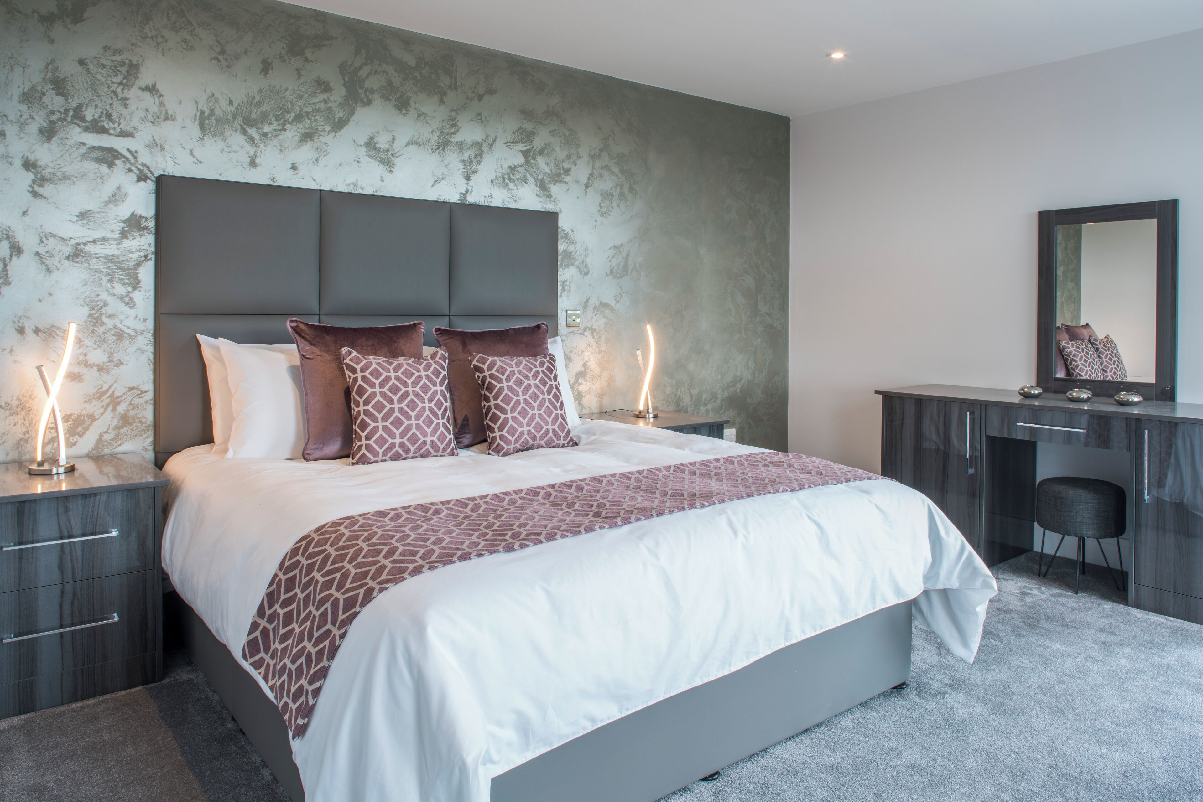 A modern bedroom with a large bed, a desk, and a chair.