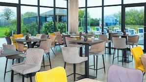 A modern dining area with large windows, outdoor seating, and a view of a glass house. - Glass House Retreat (Upminster)