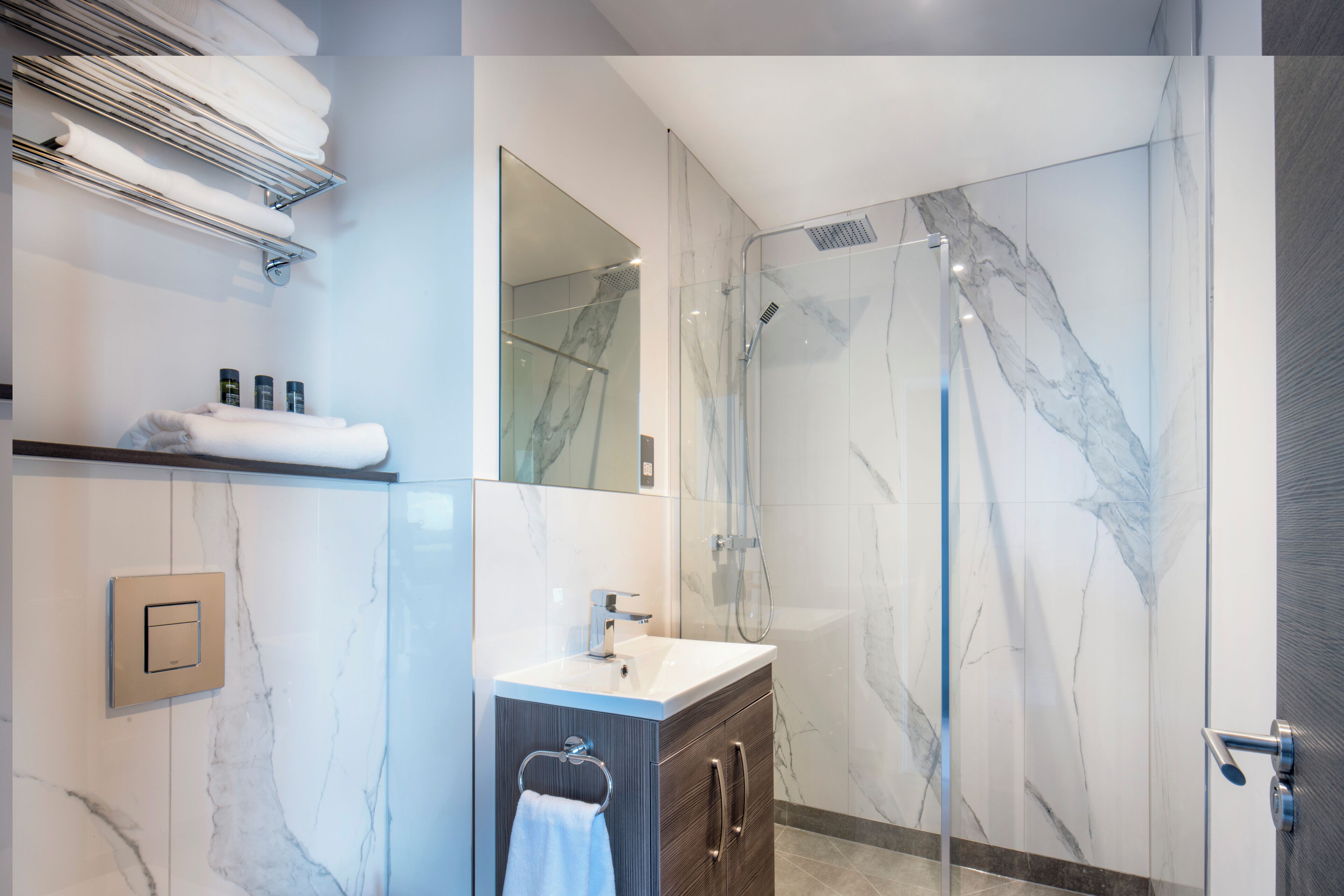 A modern bathroom with a glass-enclosed shower, marble walls, a vanity with a sink, and neatly arranged towels.