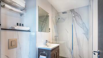 A modern bathroom with a glass-enclosed shower, marble walls, a vanity with a sink, and neatly arranged towels.