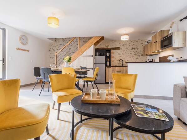A modern living room with yellow chairs, a black coffee table, and a dining area with a wooden staircase.