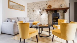 A cozy living room with a stone wall, a fireplace, a sofa, and yellow chairs.