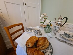 Une table à manger dressée avec une assiette de pâtisseries, une carafe, des tasses et un vase rempli de fleurs.