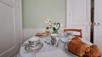 A dining table set with white tablecloth, plates, cups, a vase with flowers, a teapot, and a loaf of bread.