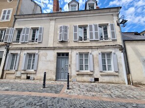 Un bâtiment historique à la façade symétrique, doté de grandes fenêtres avec volets et d’une porte centrale.