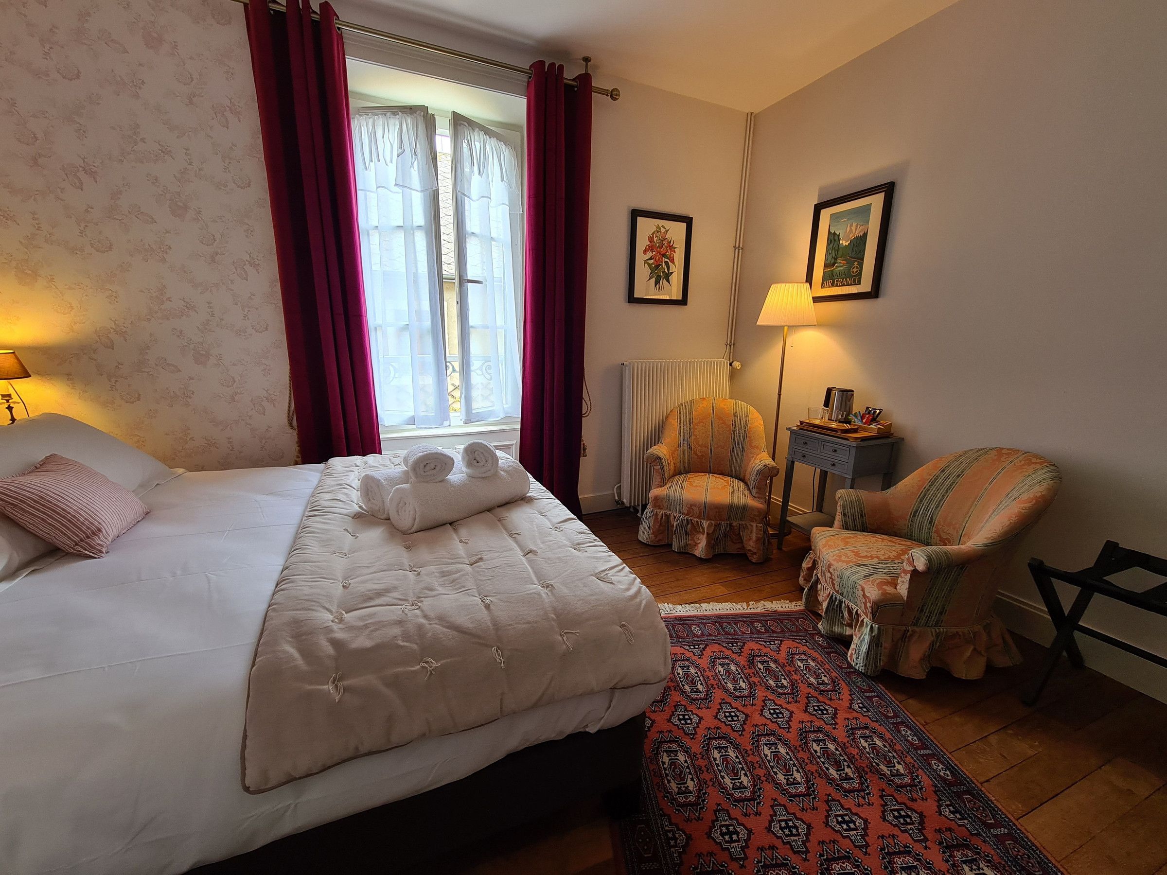 A hotel room with a bed, a chair, a small table, a lamp, and a window with curtains.