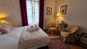 Ein Hotelzimmer mit Bett, Sessel, Nachttisch, Lampe und einem fensterbepflanzten Fenster.