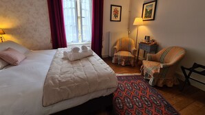 A hotel room with a bed, a chair, a small table, a lamp, and a window with curtains. - Cozy Room "Toscane" with Private Bath, 1st Floor, Breakfast Included, Central Châteauroux (Châteauroux)
