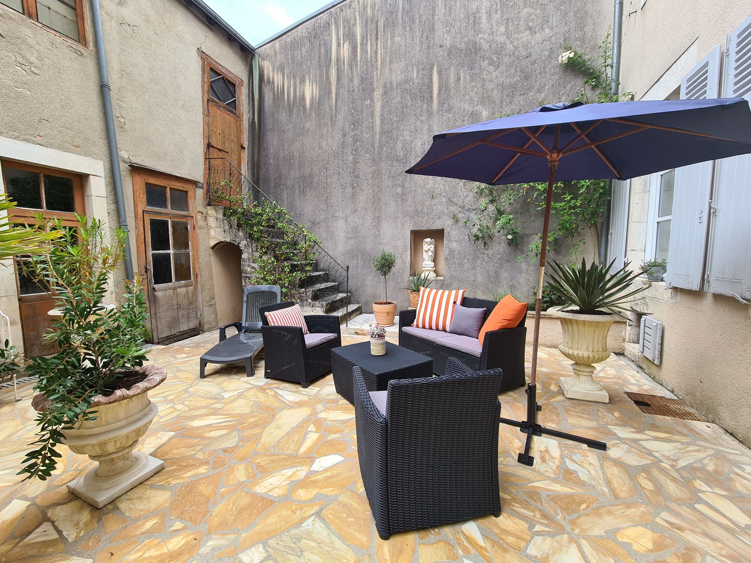 Une terrasse extérieure avec des meubles en osier, un sol en pierre et des plantes en pot.