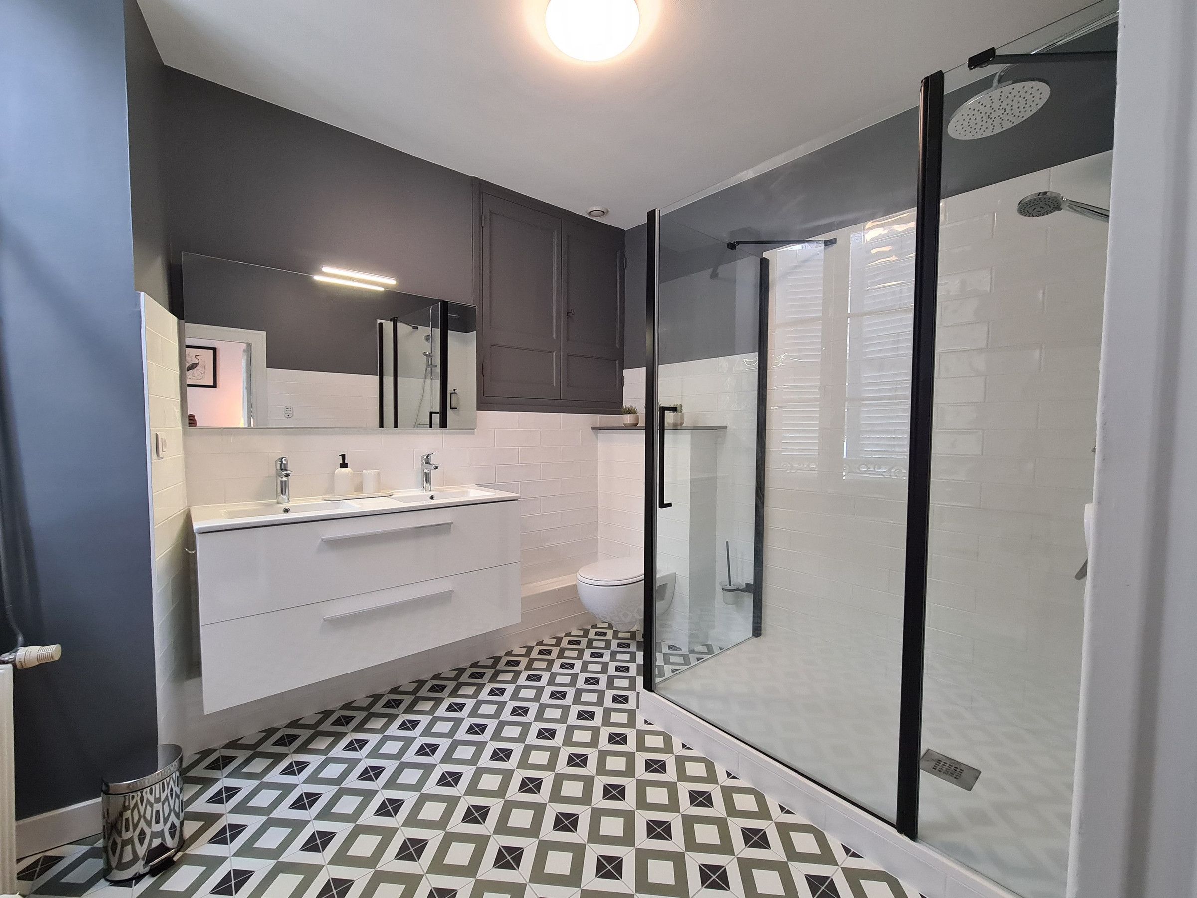 Een moderne badkamer met een douchecabine van glas, een wit wastafelmeubel met een spiegel erboven en vloertegels met een patroon.