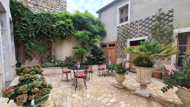 A courtyard with stone flooring, a table with chairs, potted plants, and a stone wall with climbing plants. - Spacieuse Chambre avec Lit King-Size, Salle d'Eau Privative et Petit-Déjeuner Inclus (Châteauroux)