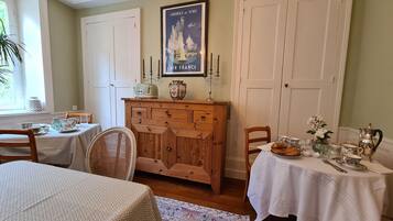 Een eetkamer met een houten kast, twee gedekte tafels en een poster aan de muur.