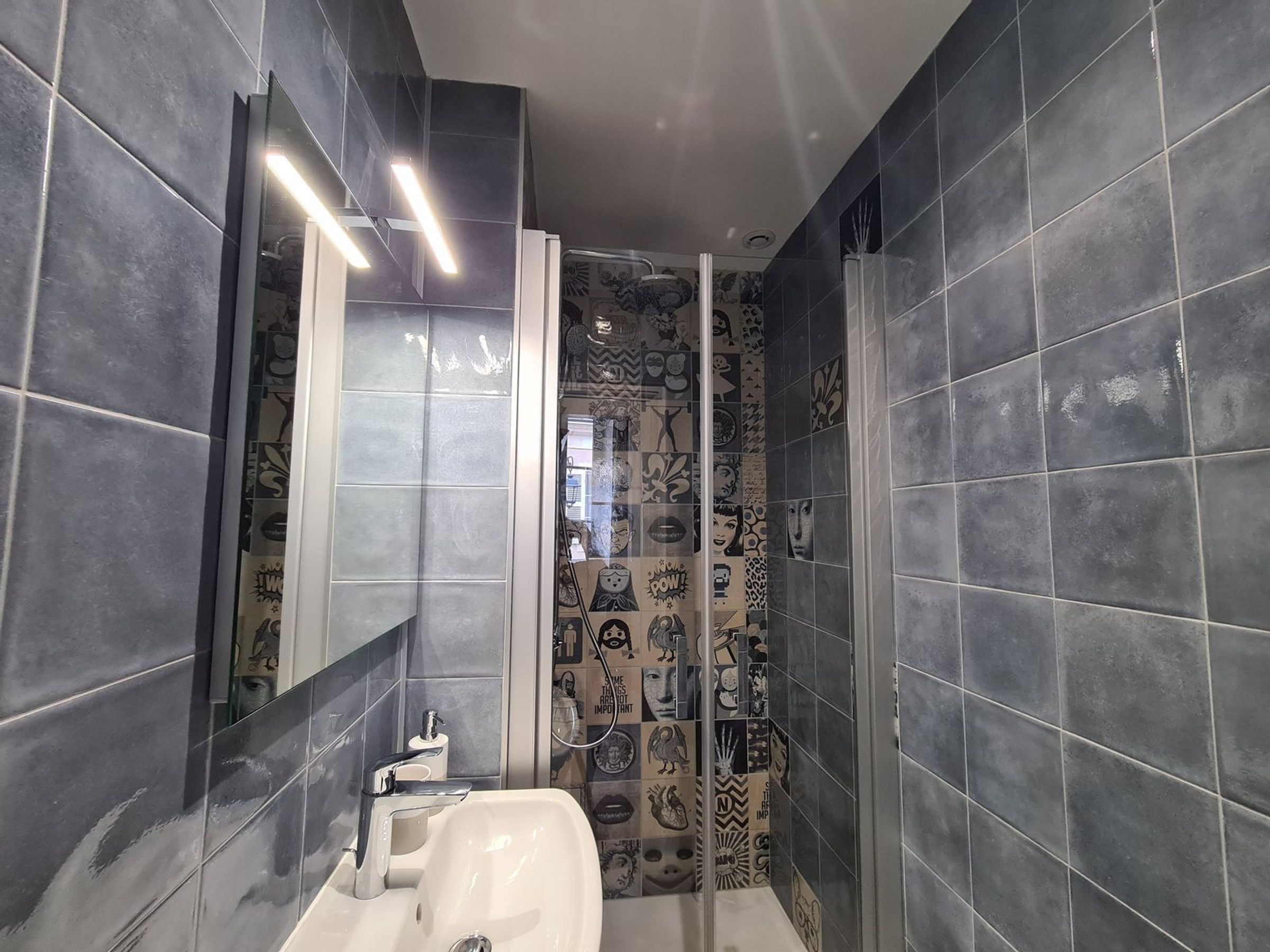 A bathroom with dark tiles, a white sink, and a mirror.
