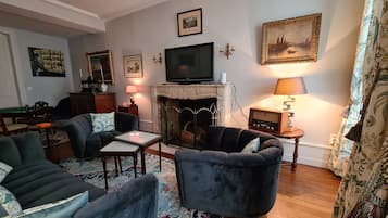 Een woonkamer met een open haard, een televisie en een tafel met stoelen.