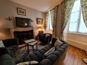 A living room with a sofa, chairs, a fireplace, a television, and a patterned rug. - Cozy Room "Pondichéry" with Private Bath and Breakfast Included in Châteauroux House (Châteauroux)