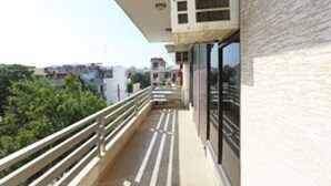 A balcony with a metal railing, a view of greenery, and a building with a textured facade. - Corporate Stay (Gurugram)