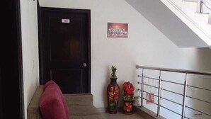 A staircase with a metal railing, a closed door with a number sign, a sofa with a red cushion, and two decorative items on the floor. - Corporate Stay (Gurugram)