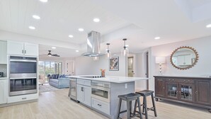 Una cocina moderna con armarios blancos, electrodomésticos de acero inoxidable y una isla central con taburetes.