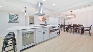 Una cocina moderna con una isla grande, electrodomésticos de acero inoxidable y un comedor con sillas de madera y una araña.