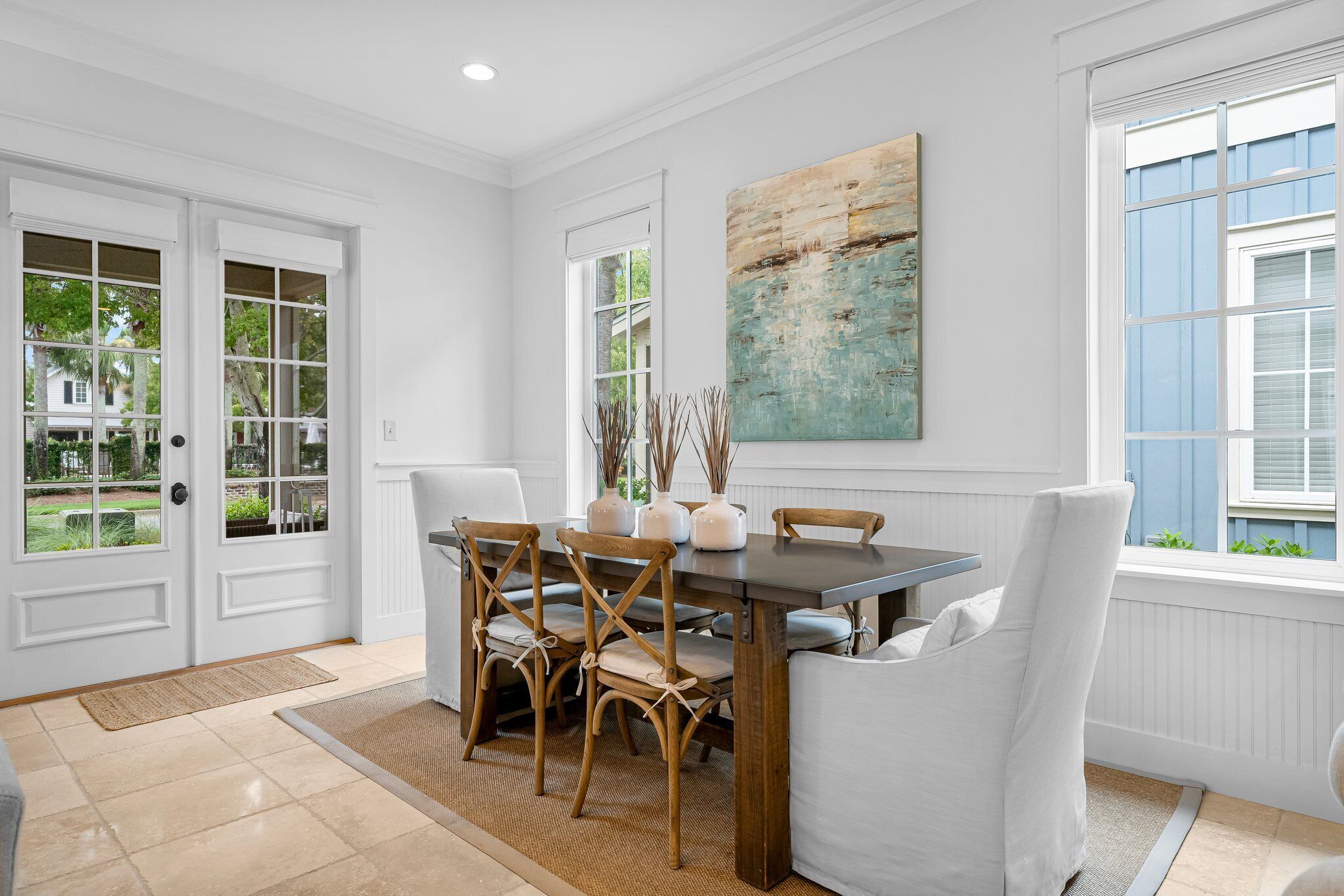Un coin repas avec une table en bois, des chaises blanches et un grand tableau accroché au mur.