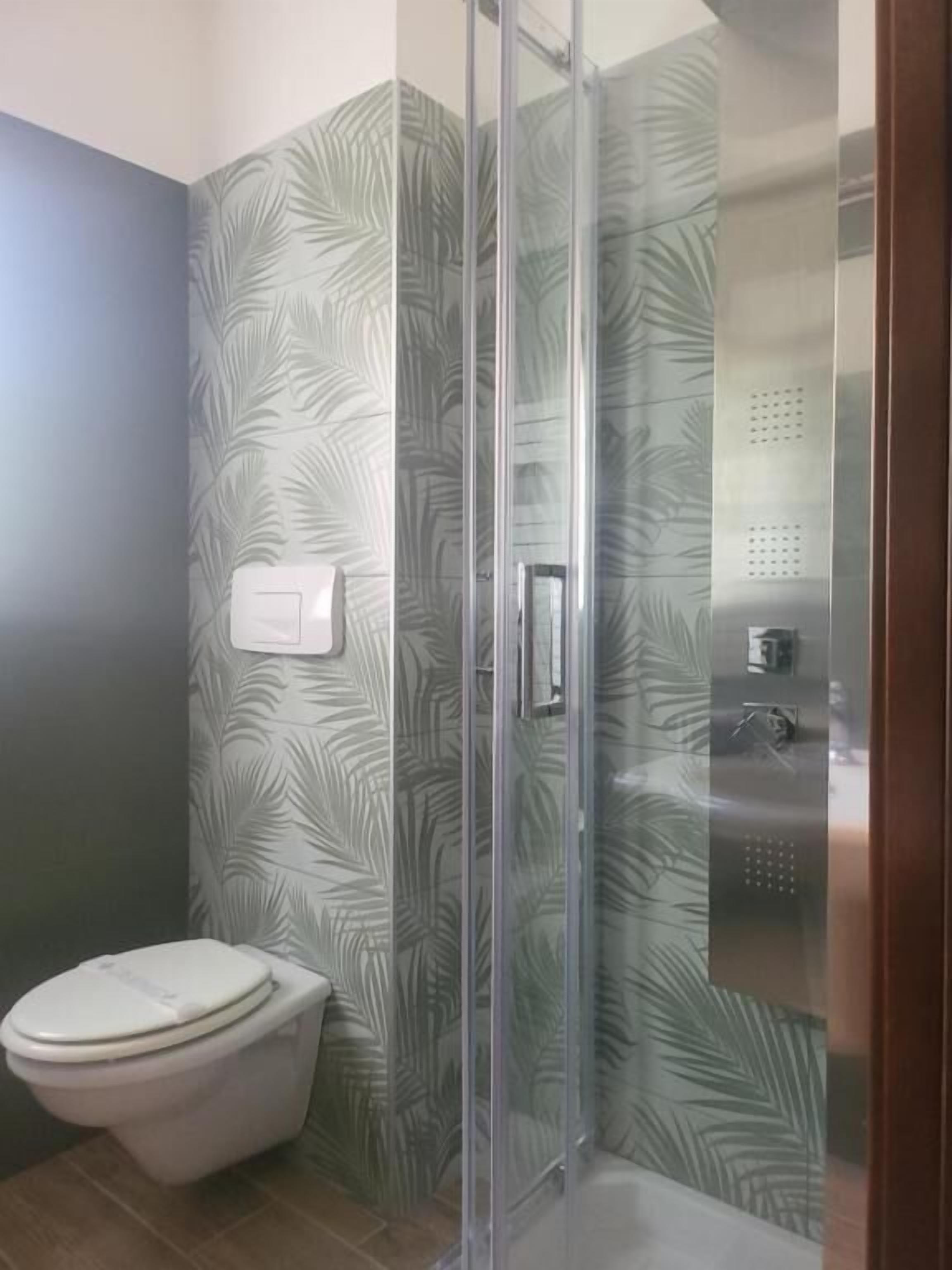 Een badkamer met toilet, douchecabine van glas en een wand met bladmotief.