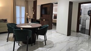 A modern living room with a round dining table, dark green chairs, a sofa, and a TV mounted on a wooden panel. - La Locanda di Castromediano (Castelmezzano)