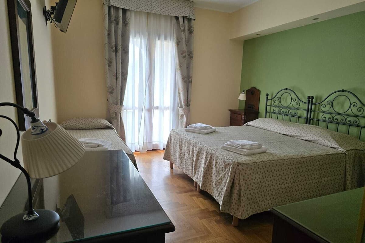 A bedroom with two beds, a desk with a lamp, a wooden nightstand, and a green wall.