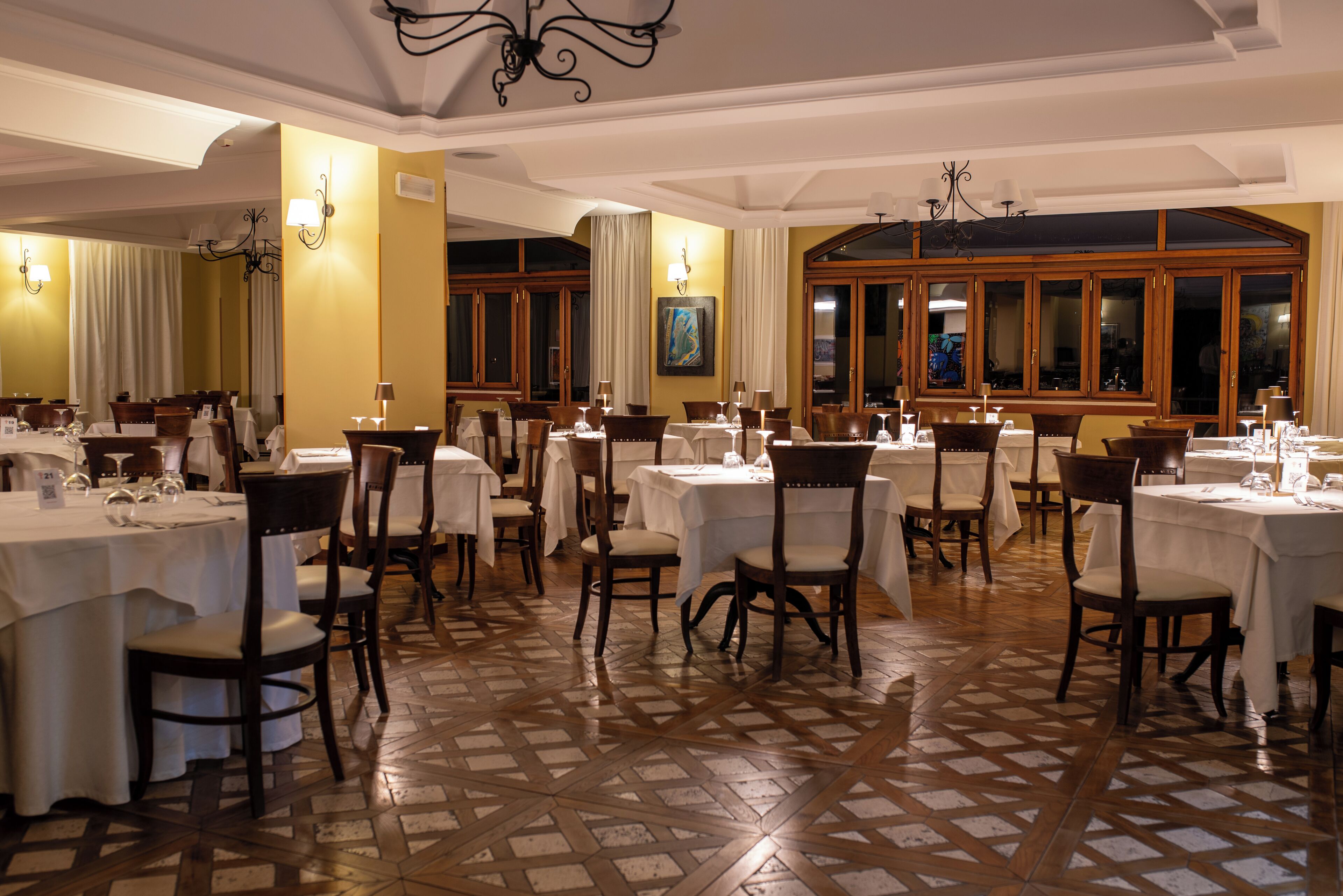 A dining area with multiple tables and chairs, wooden flooring, and large windows.