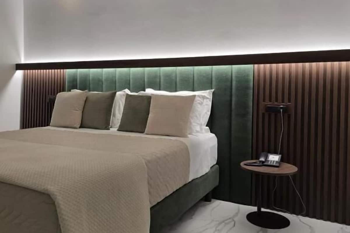 A modern bedroom with a large bed, a headboard with vertical slats, a bedside table with a lamp, and a marble floor.