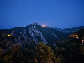 A mountainous landscape at dusk with a prominent rocky peak and a small settlement with lights. - La Locanda di Castromediano (Castelmezzano)