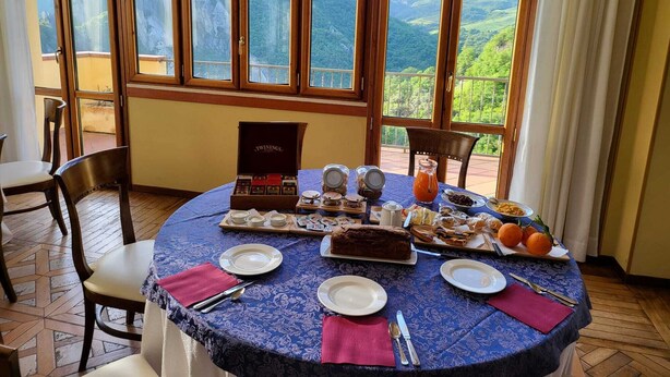 A dining table set with plates, cutlery, and a variety of food items, positioned in a room with large windows offering a scenic view of hills. - La Locanda di Castromediano (Castelmezzano)