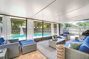 Relax in this serene sunroom with a backyard pool view, featuring wicker furniture and a cozy seating area.