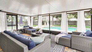A covered patio area with wicker furniture, a small table, and a view of a backyard swimming pool. - Screened Lanai + Fenced Yard: Luxe Orlando Home (Orlando)