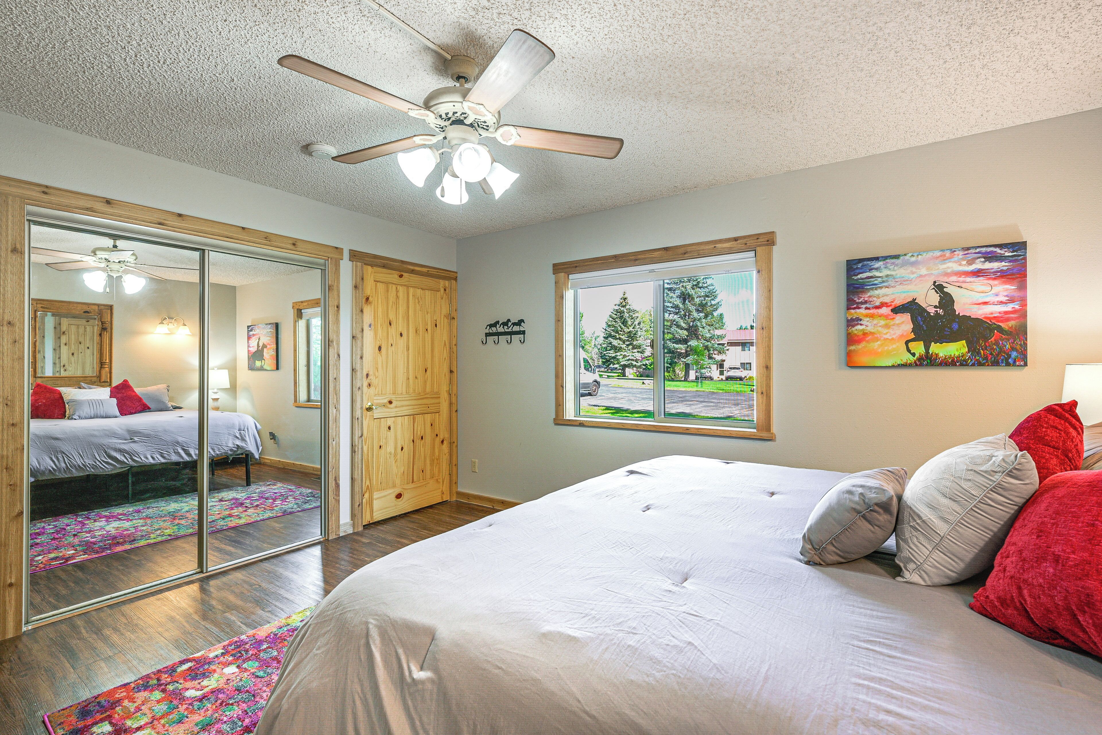 A bedroom with a bed, a ceiling fan, a large window, and a painting on the wall.