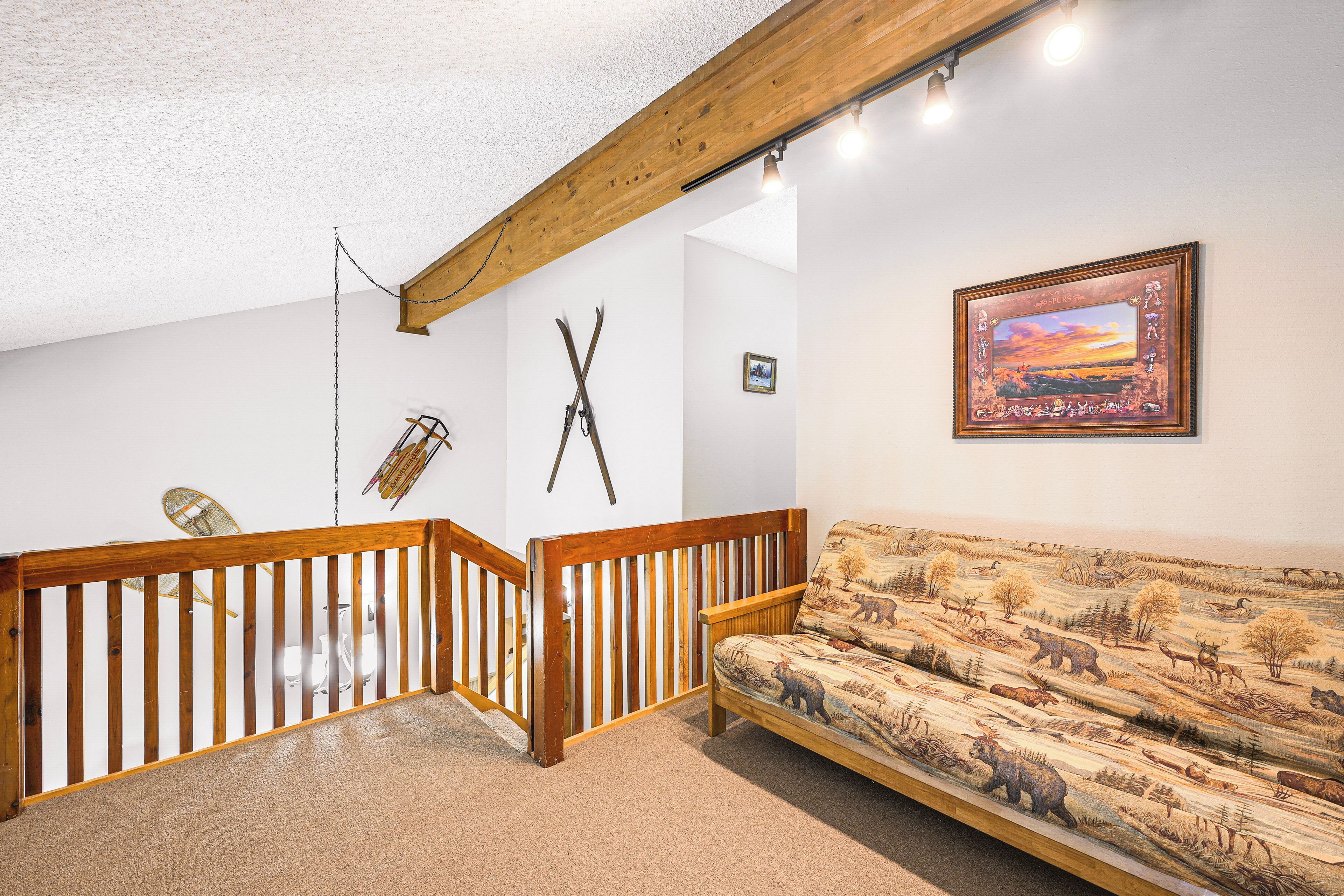 Une pièce avec un escalier en bois, un canapé orné d’un motif inspiré de la nature, un tableau encadré et un porte-skis fixé au mur.