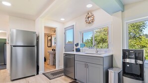 A modern kitchen with a stainless steel refrigerator, grey cabinets, a water dispenser, and a view of the outdoors through a window. - 1/2 Mi to Ocean: Copalis Beach Hideaway! (Copalis Beach)