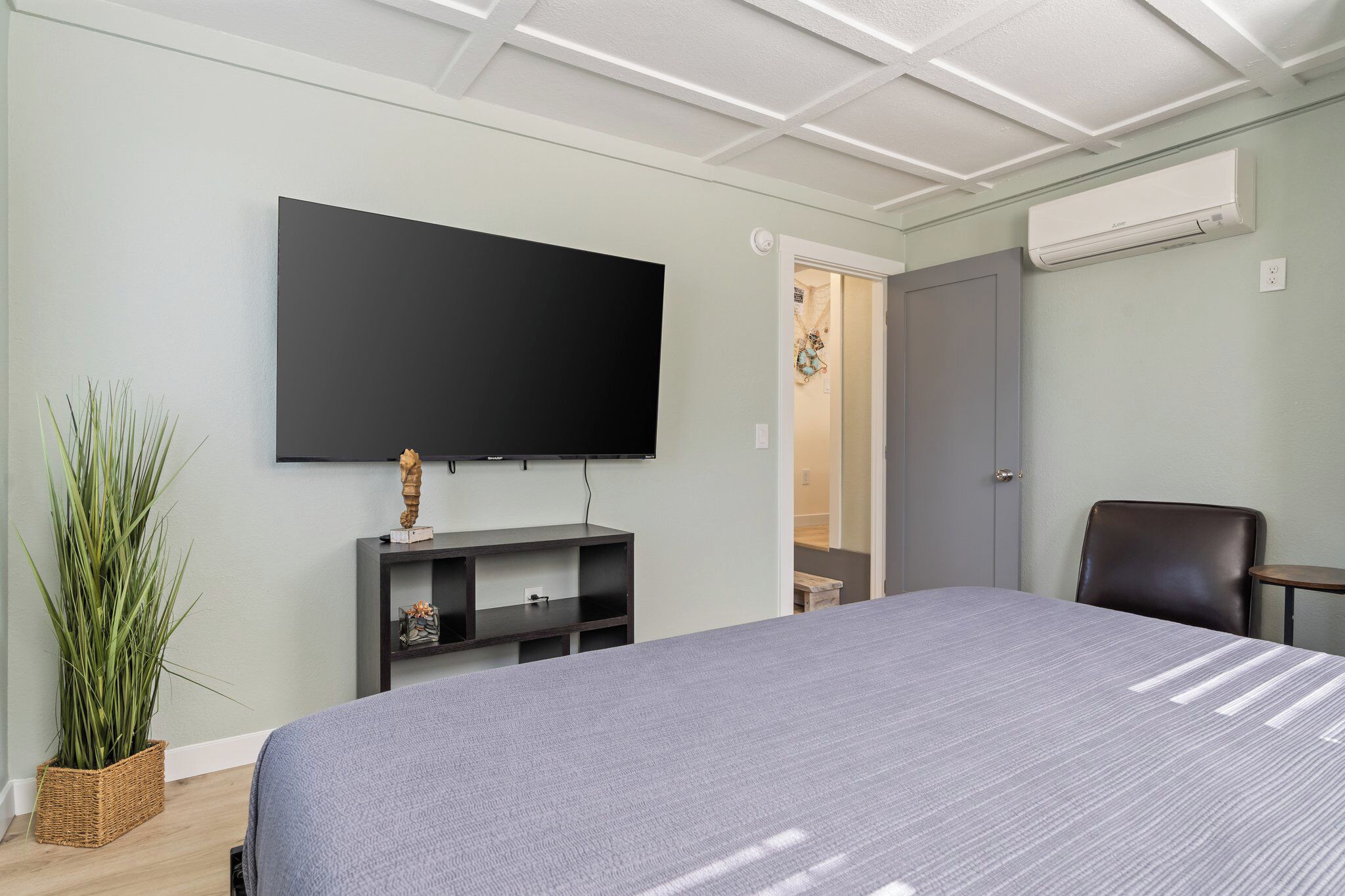 Une chambre d’hôtel équipée d’un lit, d’un téléviseur à écran plat fixé au mur, d’un petit bureau, d’une chaise et d’un appareil de climatisation.