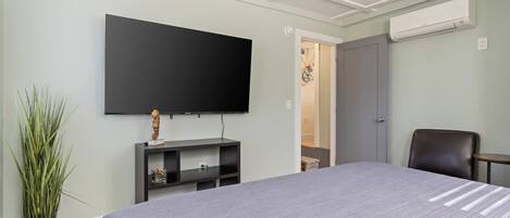 Une chambre d’hôtel équipée d’un lit, d’un téléviseur à écran plat fixé au mur, d’un petit bureau, d’une chaise et d’un appareil de climatisation.