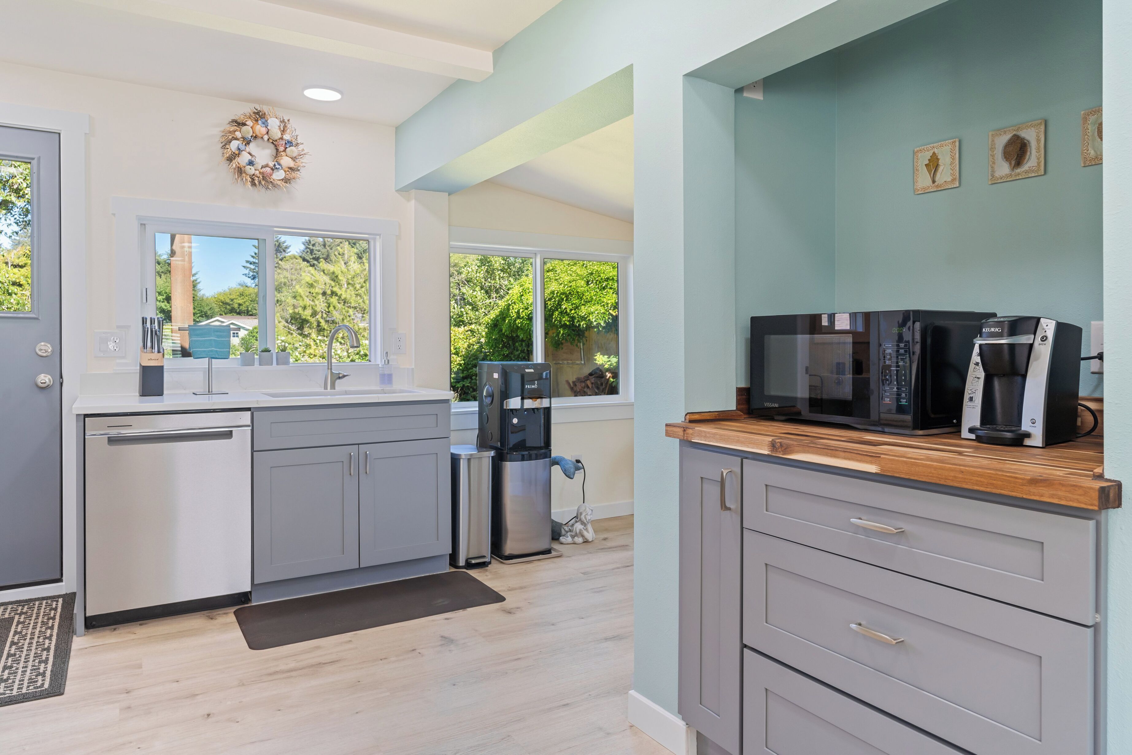 A modern kitchen with grey cabinets, a dishwasher, a water dispenser, and a microwave.