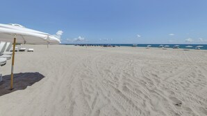A beach with white umbrellas and lounge chairs, a clear sky, and footprints in the sand. - Ocean Views & Pool Access: Riviera Beach Condo! (Singer Island)