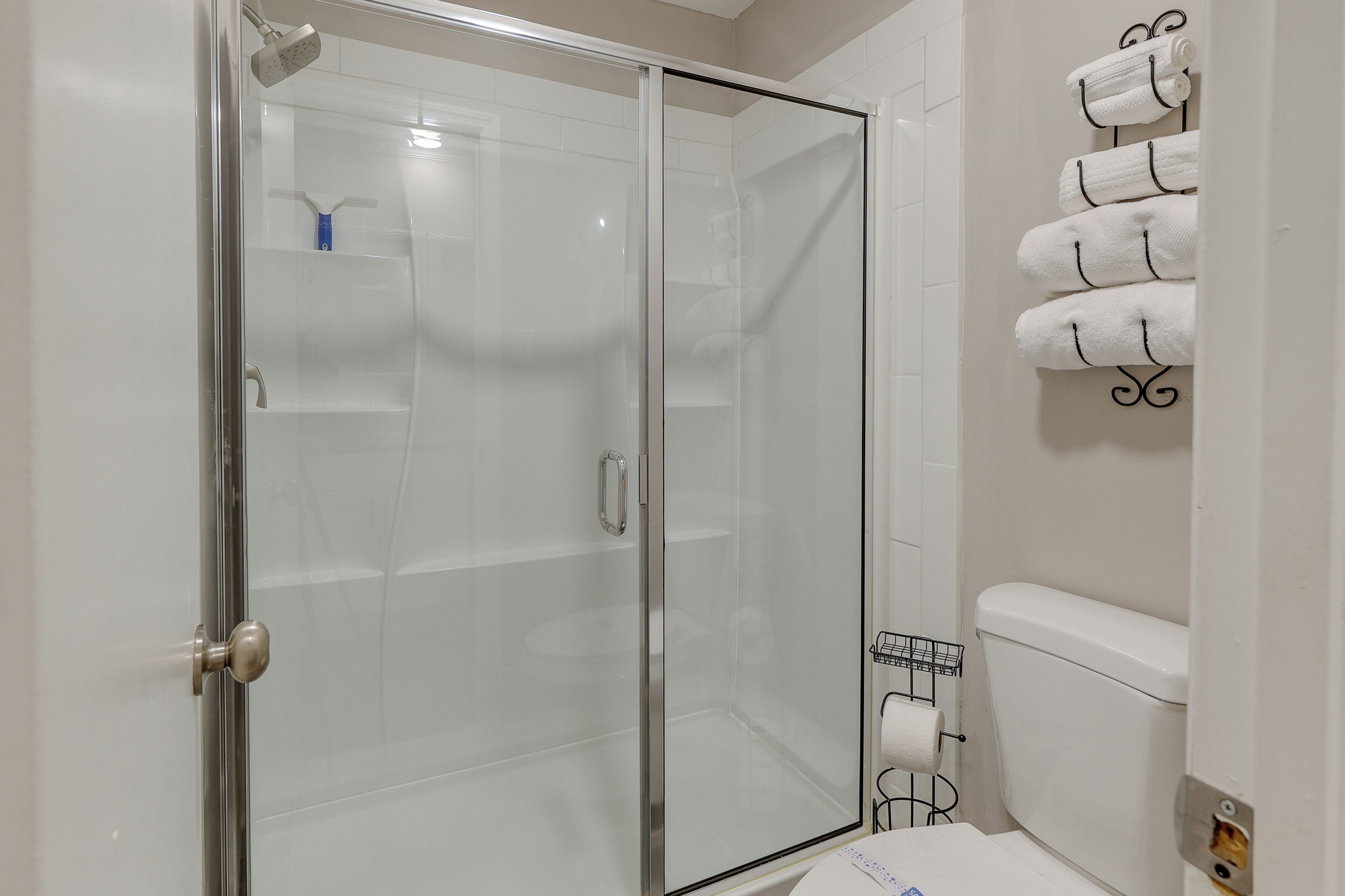Een badkamer met een douchecabine van glas, een toilet en een handdoekrek met meerdere handdoeken.