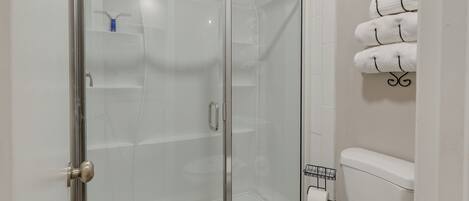 Een badkamer met een douchecabine van glas, een toilet en een handdoekrek met meerdere handdoeken.