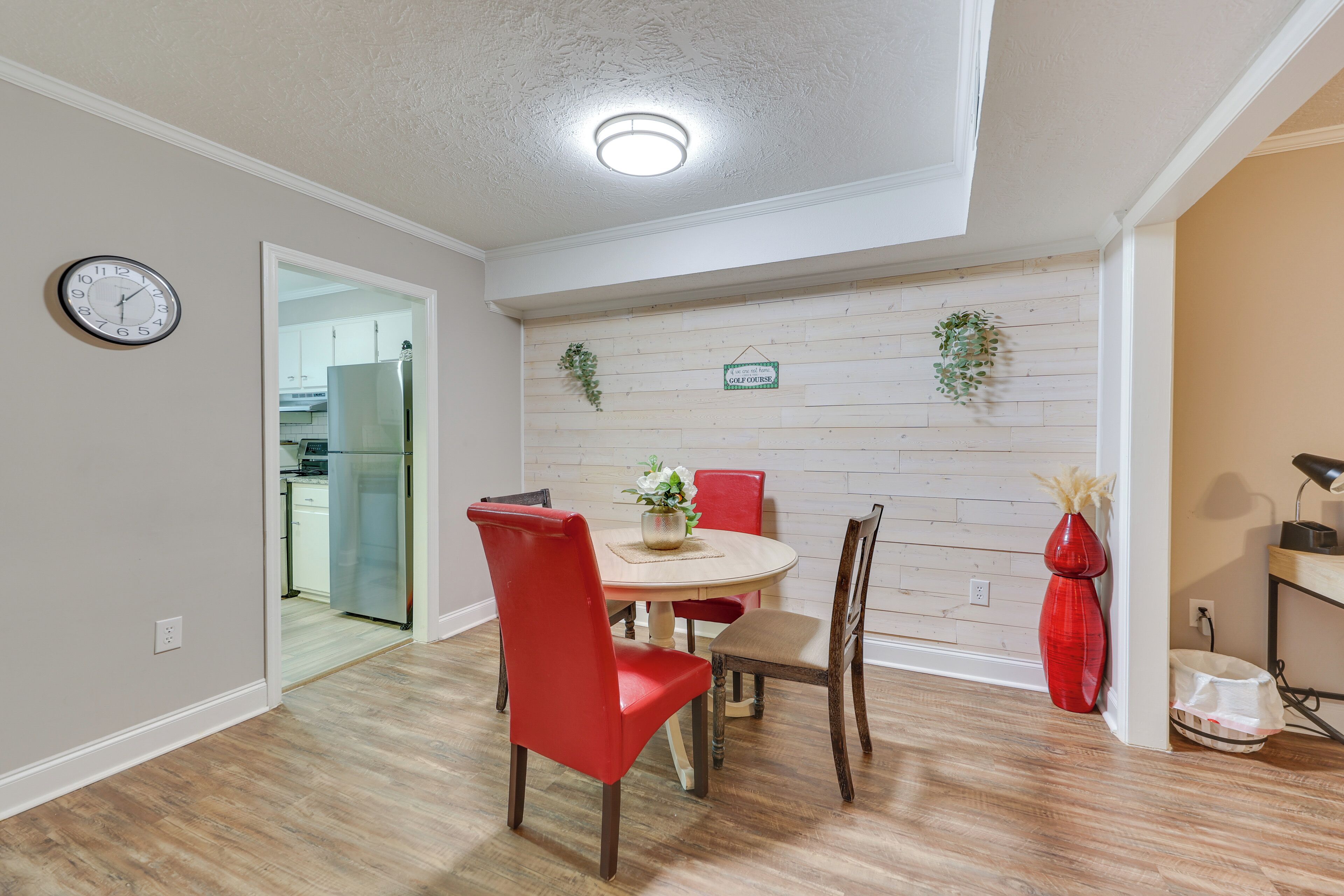 A dining area with a round table, red chairs, a clock on the wall, and a wooden wall panel.