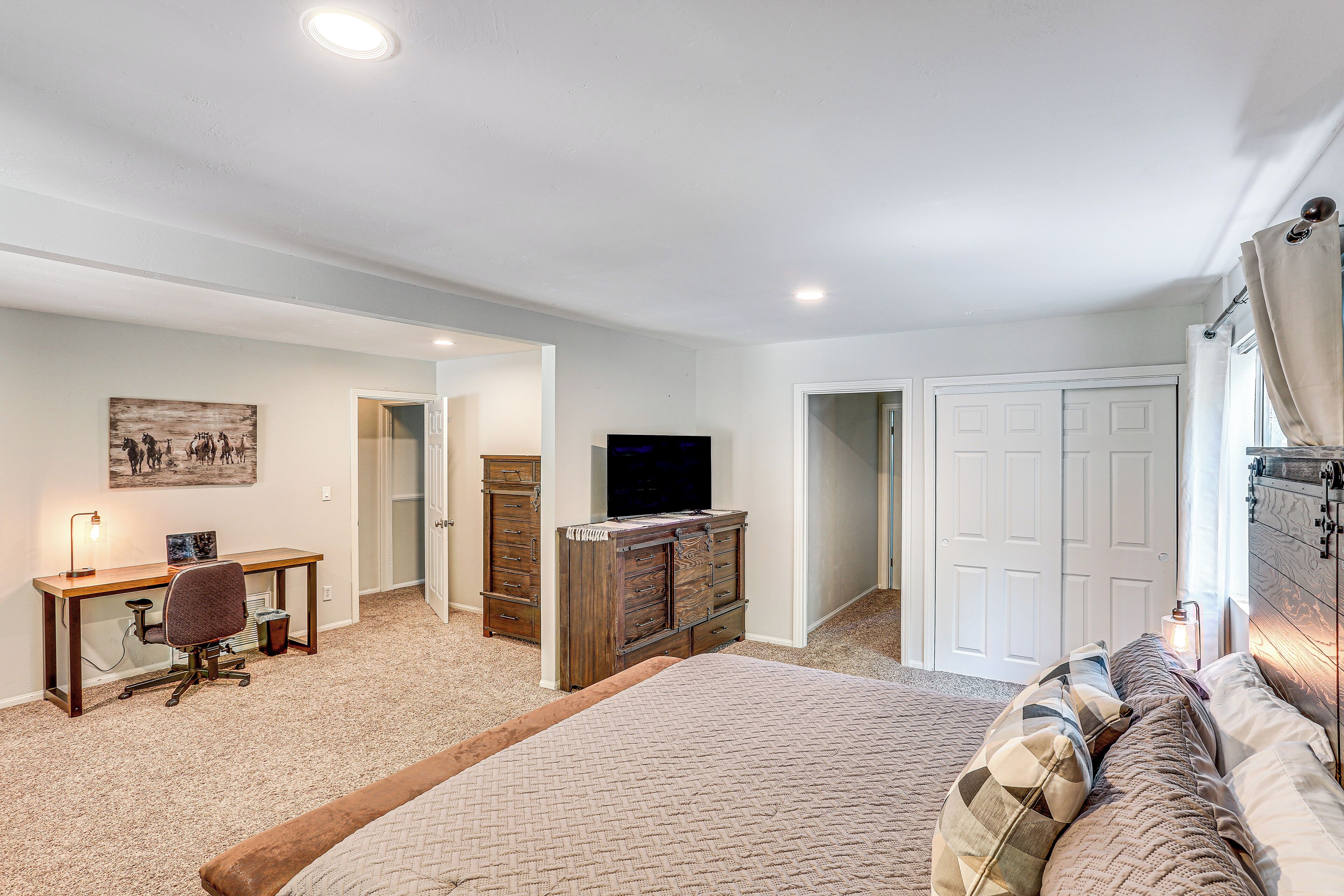 A bedroom with a bed, a desk, a chair, a dresser, a television, and a door.