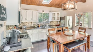 A kitchen with white cabinets, a wooden dining table, and a coffee maker. - 1 Mi to Lake: Crestline Cabin w/ Deck + Gas Grill! (Crestline)